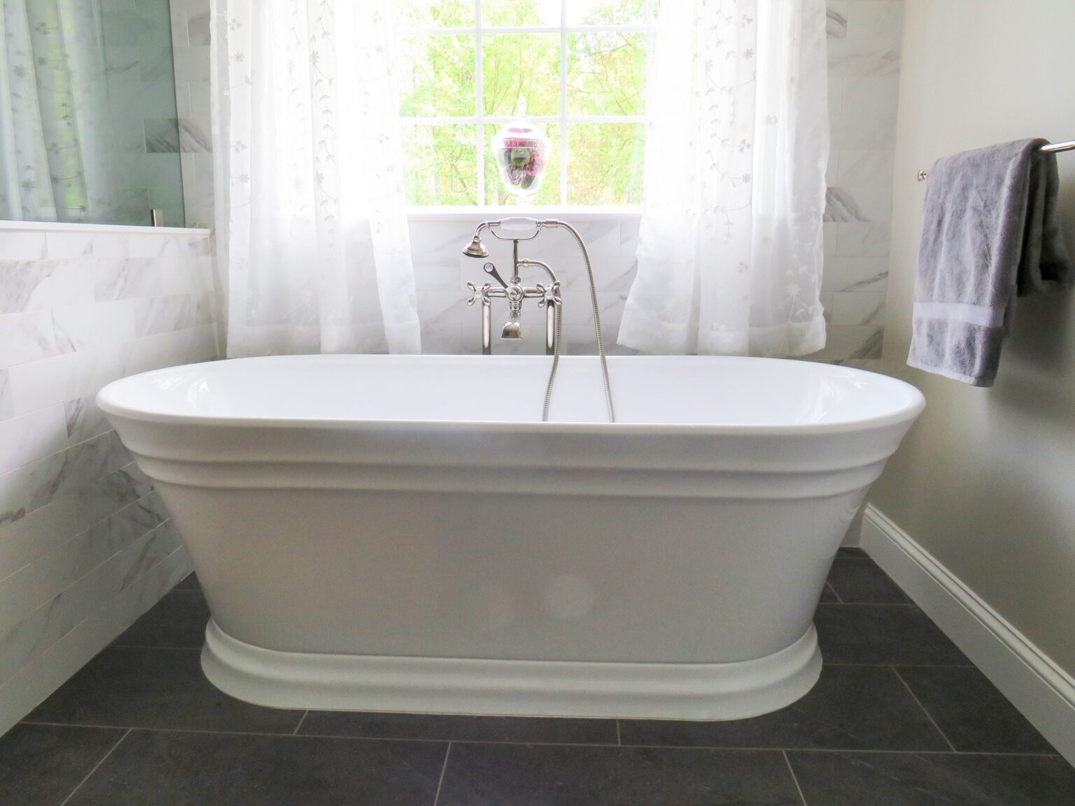 Freestanding tub under a window with marble look walls and dark tile floor, bathroom remodeling in Winchester, VA