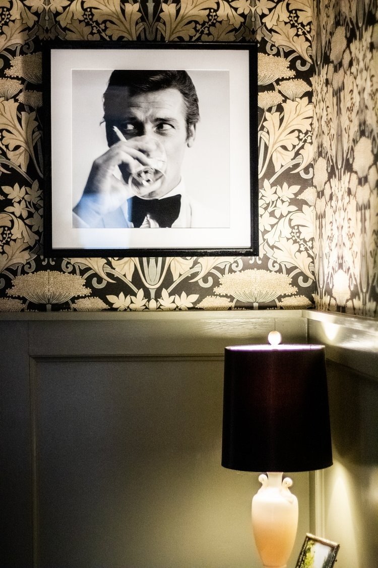 Powder room with bold patterned wallpaper, dark wainscoting and a table lamp, interior design in Winchester, VA